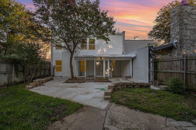 back of house at dusk with a patio area, a fenced backyard, and a yard