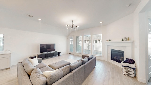 living room featuring light wood finished floors, visible vents, a notable chandelier, and a stone fireplace