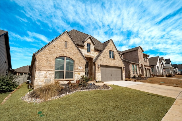 french country home with brick siding, an attached garage, stone siding, driveway, and a front lawn