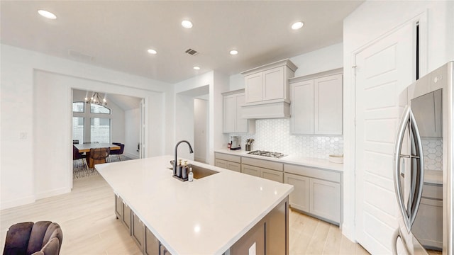 kitchen featuring visible vents, an island with sink, appliances with stainless steel finishes, a sink, and backsplash