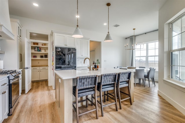 kitchen with stainless steel gas range oven, black built in refrigerator, a center island with sink, and pendant lighting