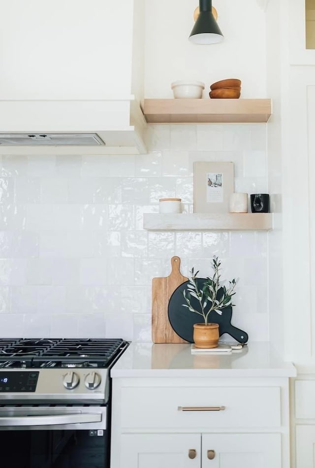 kitchen with white cabinets, light countertops, stainless steel gas range oven, and decorative backsplash