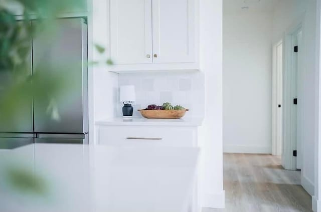 interior space with light wood-type flooring, baseboards, decorative backsplash, and stainless steel refrigerator