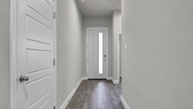 doorway featuring dark wood-style flooring, a textured wall, and baseboards