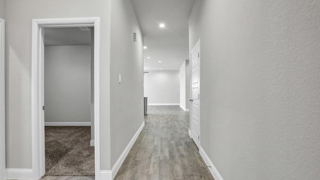 corridor with recessed lighting, a textured wall, baseboards, and wood finished floors