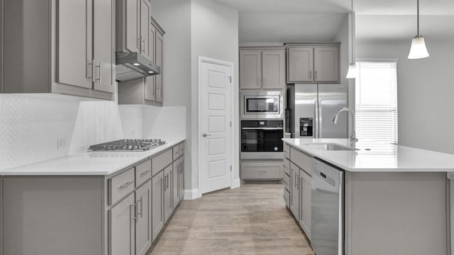 kitchen featuring gray cabinetry, under cabinet range hood, light countertops, appliances with stainless steel finishes, and hanging light fixtures