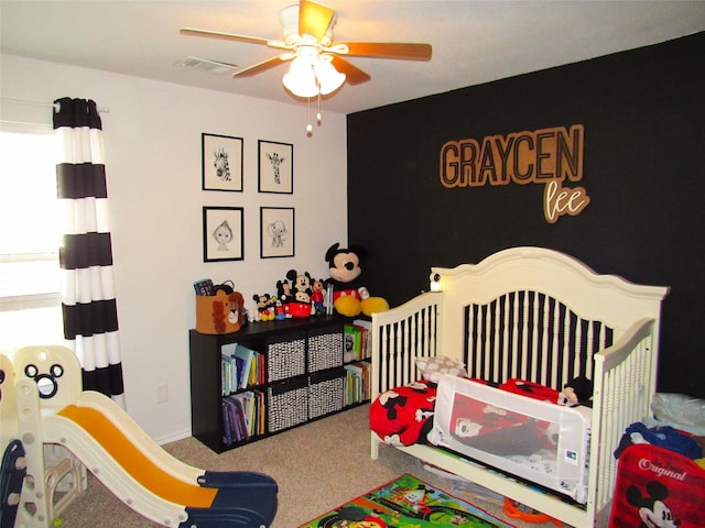 carpeted bedroom featuring a ceiling fan, a nursery area, and visible vents