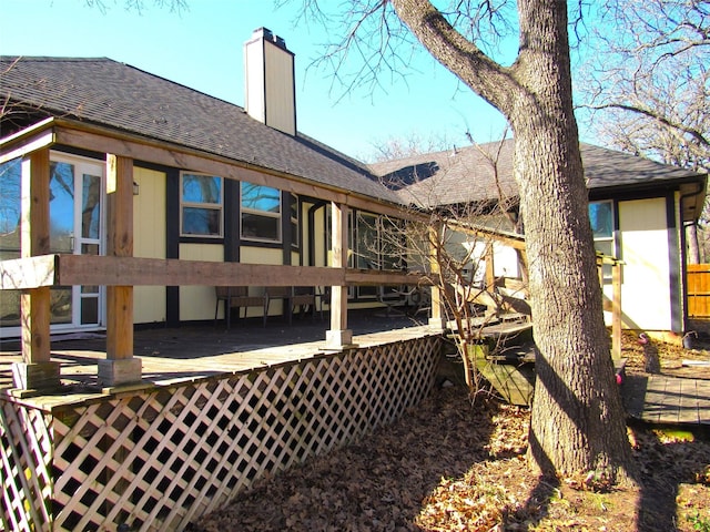 rear view of house featuring a deck, roof with shingles, and a chimney