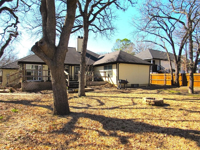 back of property with an outdoor fire pit, a chimney, fence, and a lawn