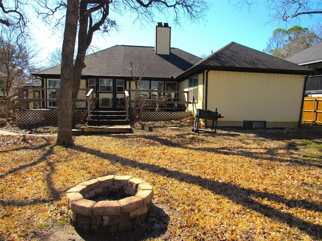 back of house with brick siding, a chimney, a shingled roof, a deck, and a fire pit