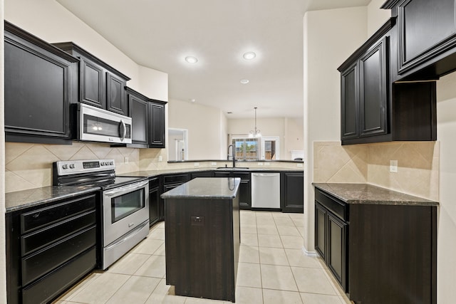 kitchen featuring a kitchen island, a peninsula, stainless steel appliances, dark cabinetry, and a sink