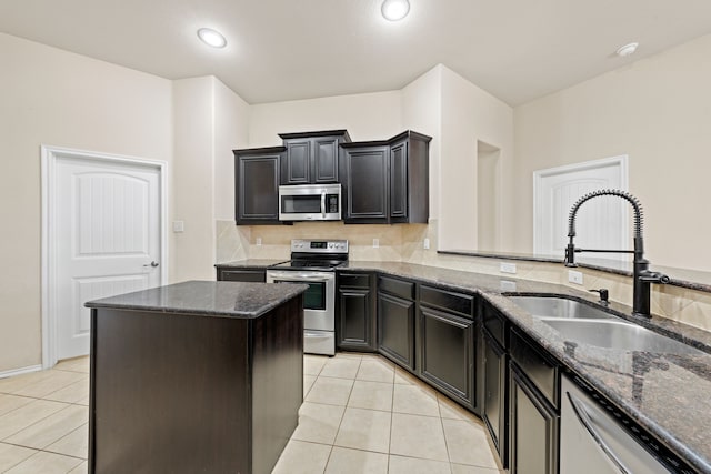 kitchen with light tile patterned floors, appliances with stainless steel finishes, a kitchen island, a sink, and dark stone counters