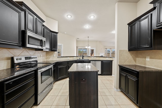 kitchen with light tile patterned flooring, a peninsula, a kitchen island, a sink, and appliances with stainless steel finishes