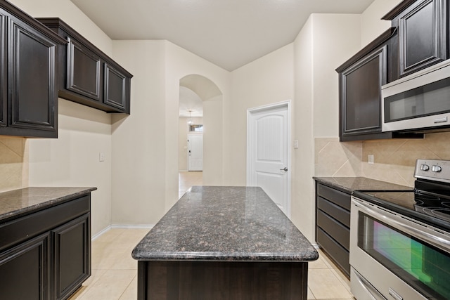 kitchen featuring tasteful backsplash, arched walkways, dark stone countertops, a center island, and stainless steel appliances