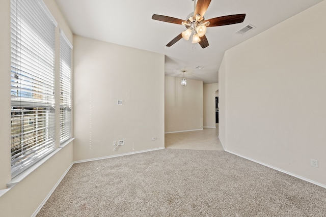 unfurnished room with a ceiling fan, light colored carpet, visible vents, and baseboards