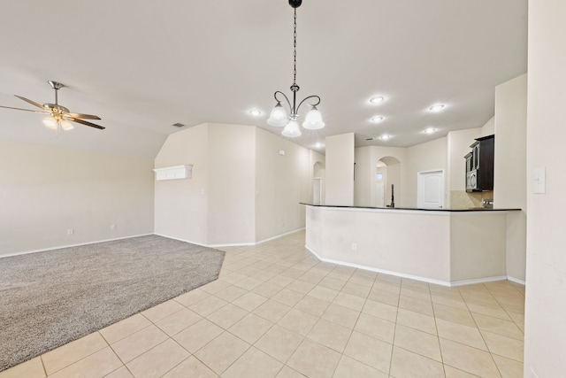 empty room with arched walkways, light tile patterned floors, light colored carpet, a ceiling fan, and baseboards