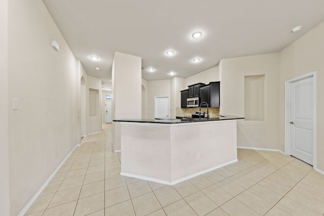 kitchen featuring light tile patterned flooring, dark cabinets, a peninsula, stainless steel appliances, and dark countertops