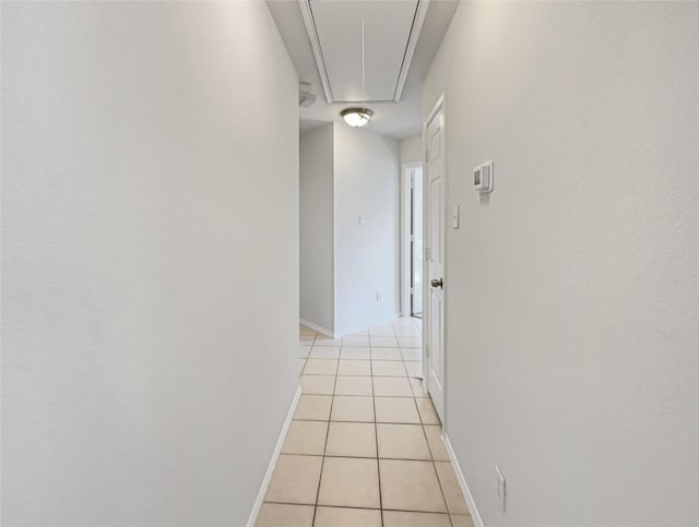 corridor featuring baseboards, attic access, and light tile patterned flooring