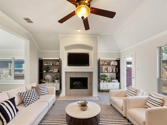 living room featuring light tile patterned floors, visible vents, a fireplace, vaulted ceiling, and crown molding