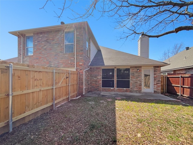 back of property featuring brick siding, a lawn, a chimney, a fenced backyard, and a patio area