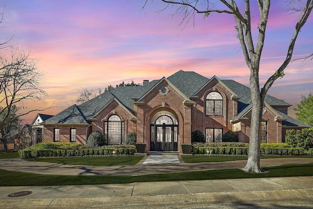 view of front of house with a chimney, french doors, a lawn, and brick siding