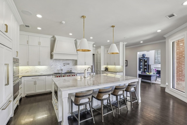 kitchen with ornamental molding, custom exhaust hood, visible vents, and white cabinets