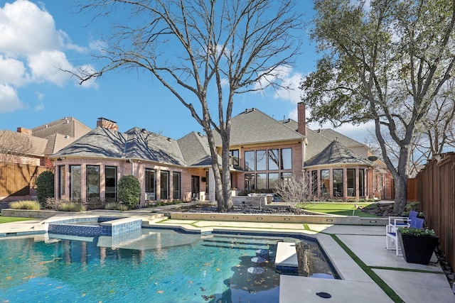 rear view of property with a chimney, fence, a patio area, a pool with connected hot tub, and brick siding