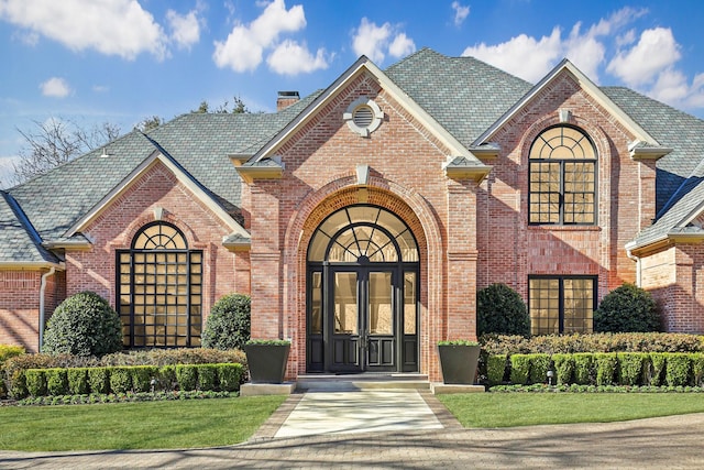 view of front of house with french doors, brick siding, a chimney, and a high end roof