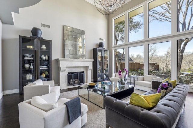 living room with visible vents, a high ceiling, an inviting chandelier, a premium fireplace, and wood finished floors