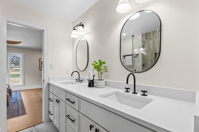 bathroom featuring a shower with shower door, a sink, baseboards, and double vanity