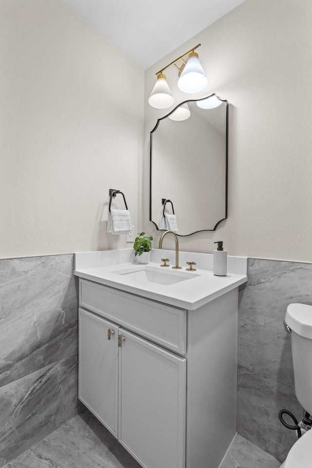 bathroom with toilet, a wainscoted wall, tile walls, and vanity