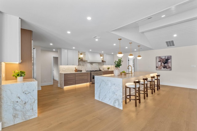 kitchen featuring white cabinetry, visible vents, decorative backsplash, light wood finished floors, and stainless steel range