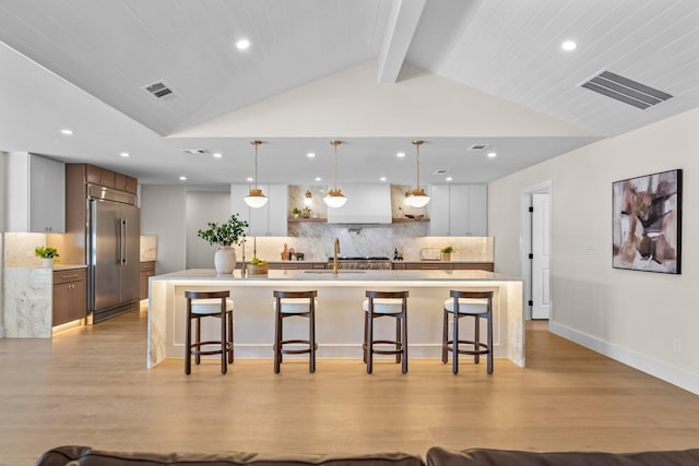 kitchen with stainless steel built in refrigerator, visible vents, lofted ceiling with beams, and a breakfast bar area