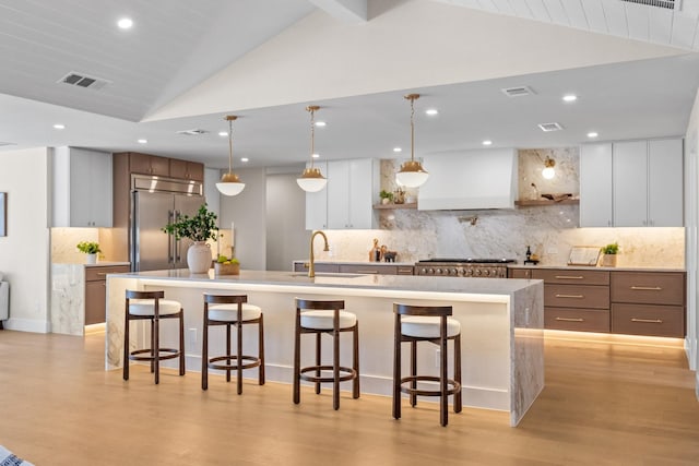 kitchen with stainless steel appliances, a sink, visible vents, vaulted ceiling, and custom range hood