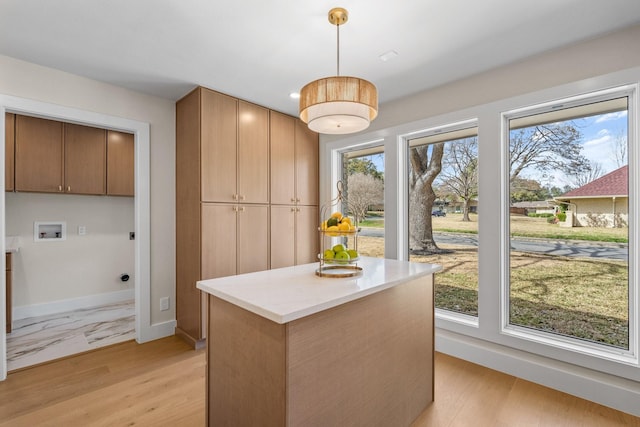 kitchen featuring baseboards, a center island, decorative light fixtures, light countertops, and light wood-style floors