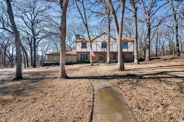 english style home with brick siding, a front lawn, and a chimney