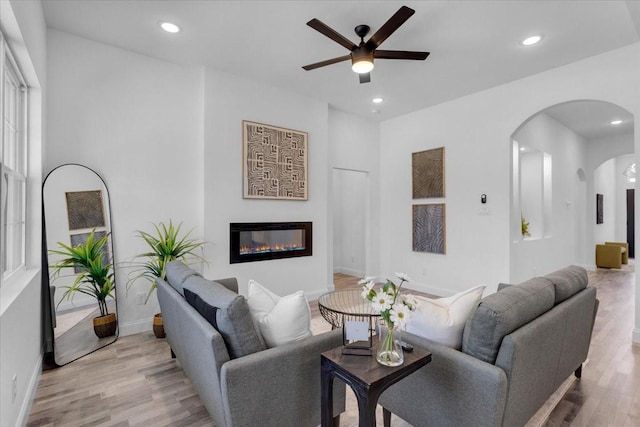 living area featuring arched walkways, a glass covered fireplace, recessed lighting, and wood finished floors