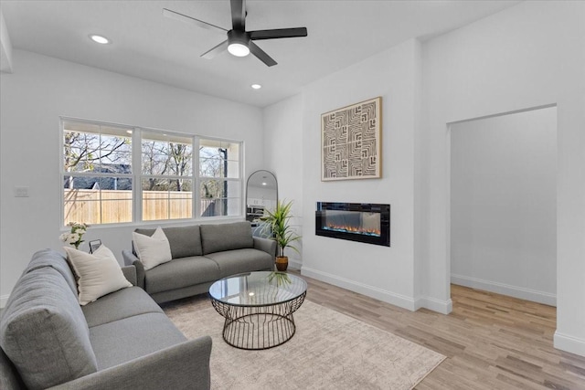 living room with light wood-style floors, recessed lighting, baseboards, and a glass covered fireplace