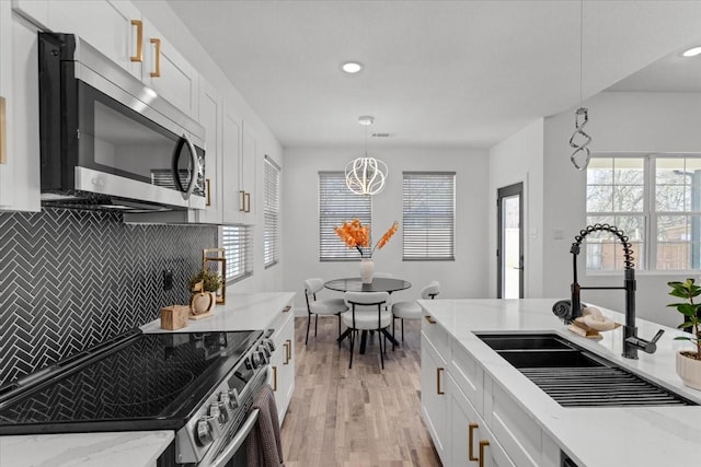 kitchen with stainless steel appliances, tasteful backsplash, light wood-style floors, white cabinetry, and a sink