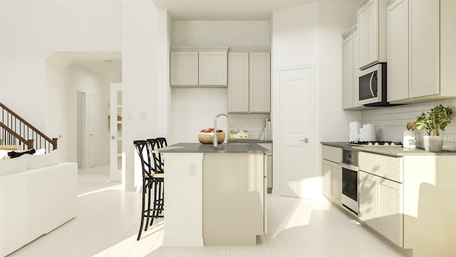 kitchen with a sink, appliances with stainless steel finishes, tasteful backsplash, dark countertops, and a center island with sink