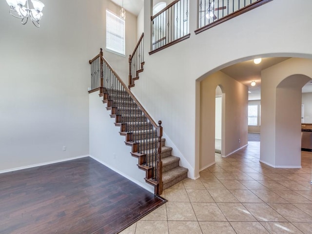 stairs with arched walkways, a towering ceiling, a chandelier, baseboards, and tile patterned floors