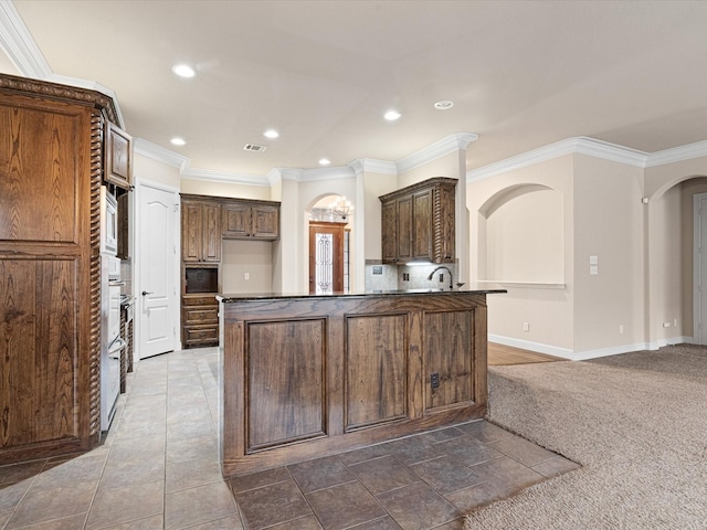 kitchen featuring arched walkways, crown molding, dark countertops, visible vents, and a peninsula