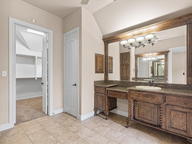 bathroom with lofted ceiling, vanity, baseboards, tile patterned floors, and a walk in closet