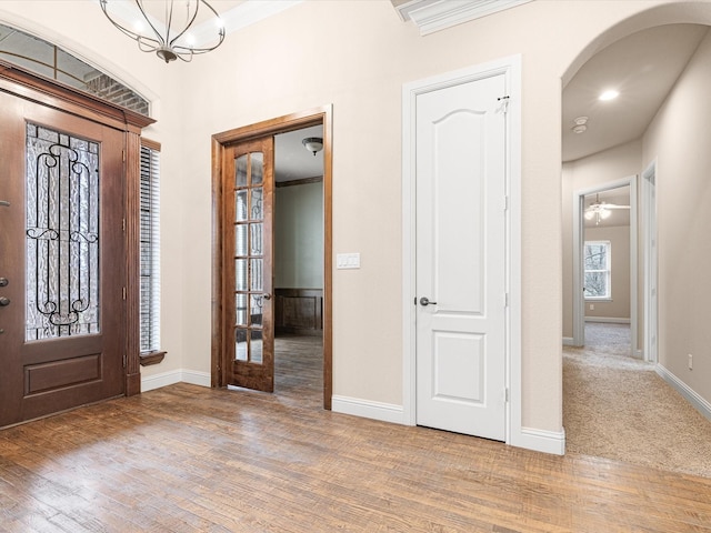 entrance foyer with arched walkways, a notable chandelier, crown molding, wood finished floors, and baseboards