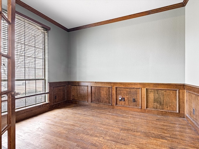 empty room with light wood-style flooring, crown molding, and wainscoting