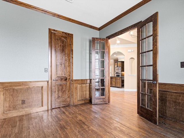 unfurnished room featuring arched walkways, a wainscoted wall, crown molding, and wood finished floors