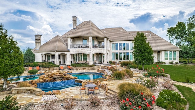 rear view of property featuring a patio, a chimney, an outdoor hot tub, a balcony, and stone siding