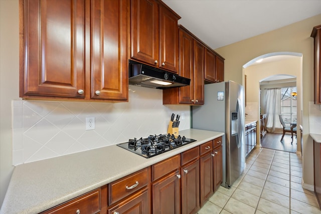 kitchen with arched walkways, tasteful backsplash, light countertops, black gas stovetop, and under cabinet range hood