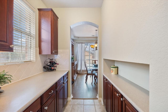 kitchen featuring arched walkways, light tile patterned floors, light countertops, hanging light fixtures, and backsplash