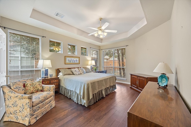 bedroom with dark wood-style floors, ceiling fan, a tray ceiling, and visible vents